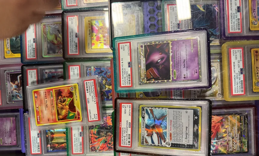 A vendor case at a show: rows of PSA slabbed Pokemon cards in colored holders, with a mint Espeon from Undaunted and a gem mint Deoxys from Holon Phantoms turned face up at the front, a mint Charizard from Stormfront beside them, and a Birthday Pikachu among the rows behind.